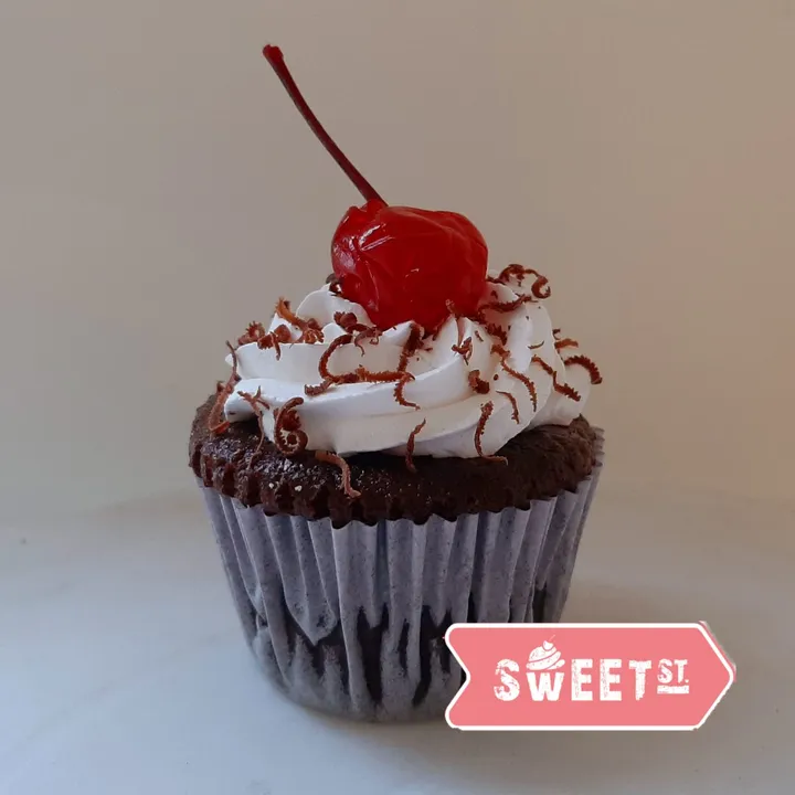 Cupcake de chocolate con crema blanca, virutas de chocolate y una cereza